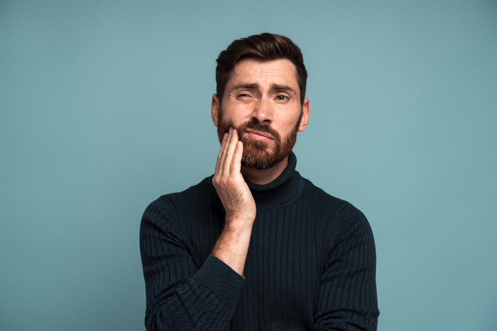 man in sweater holding face with hand | tooth extraction allentown pa