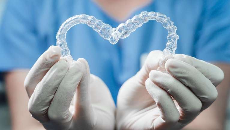 A dentist holding Invisalign trays in the shape of a heart